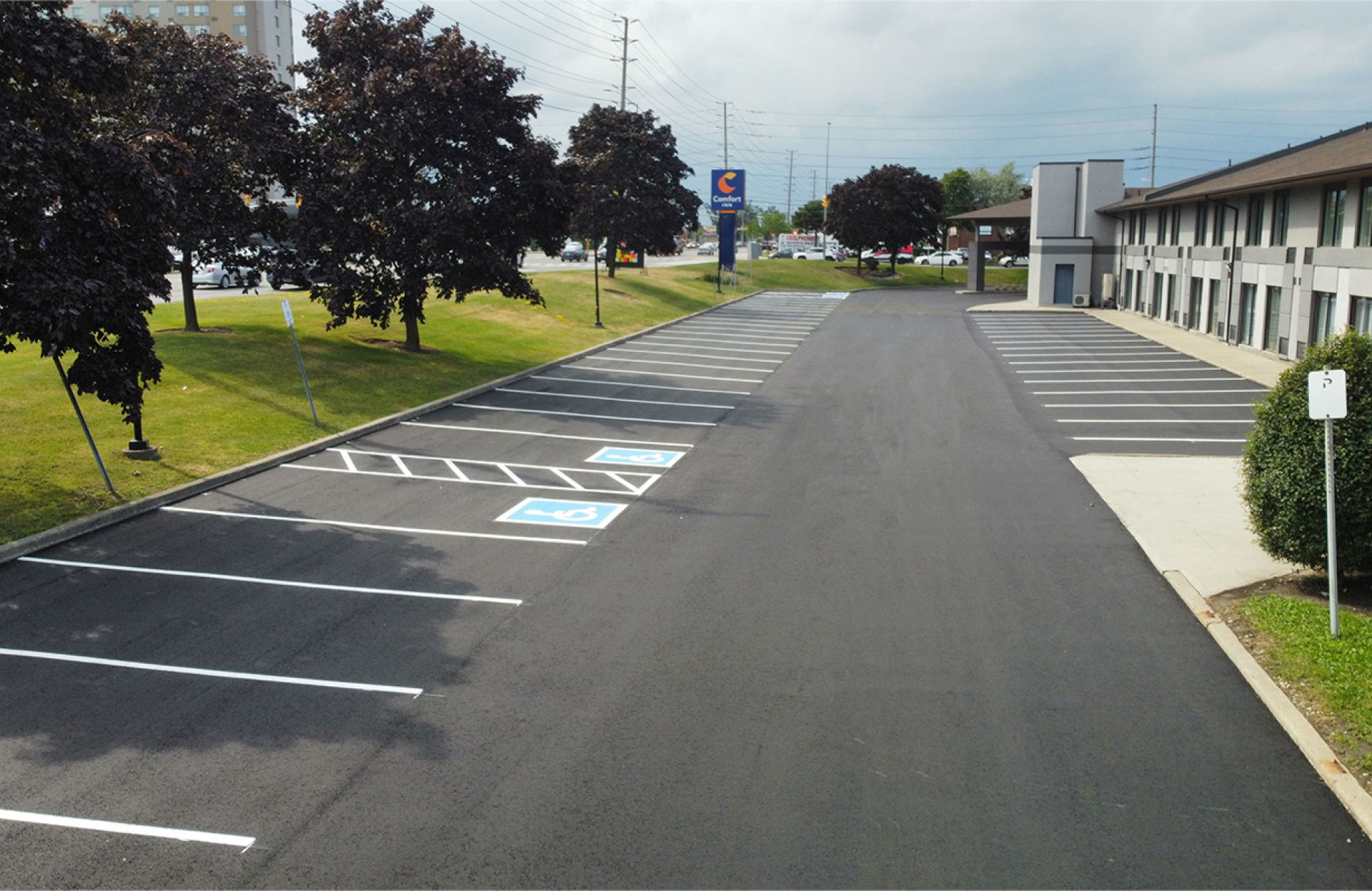 Seal Canada An empty hotel parking lot with clearly marked parking spaces, including several accessible parking spots near the building entrance. Asphalt & Coatings
