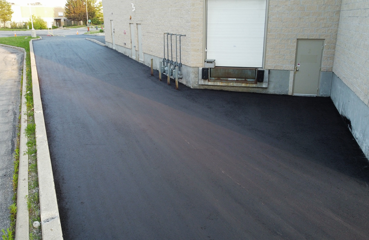 Seal Canada Freshly paved asphalt driveway next to a commercial building with utility meters, a loading dock, and a closed door. Asphalt & Coatings