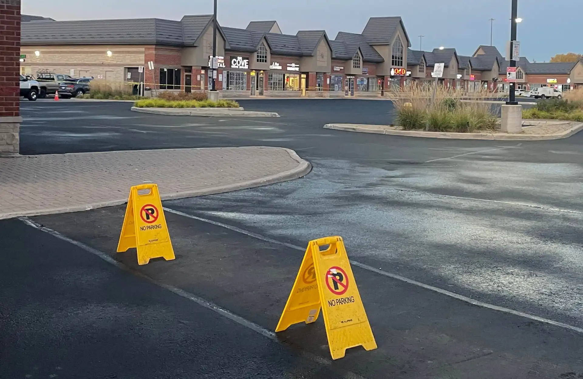Seal Canada Two yellow "No Parking" signs are placed on an empty parking lot near a strip mall with shops in the background. Asphalt & Coatings