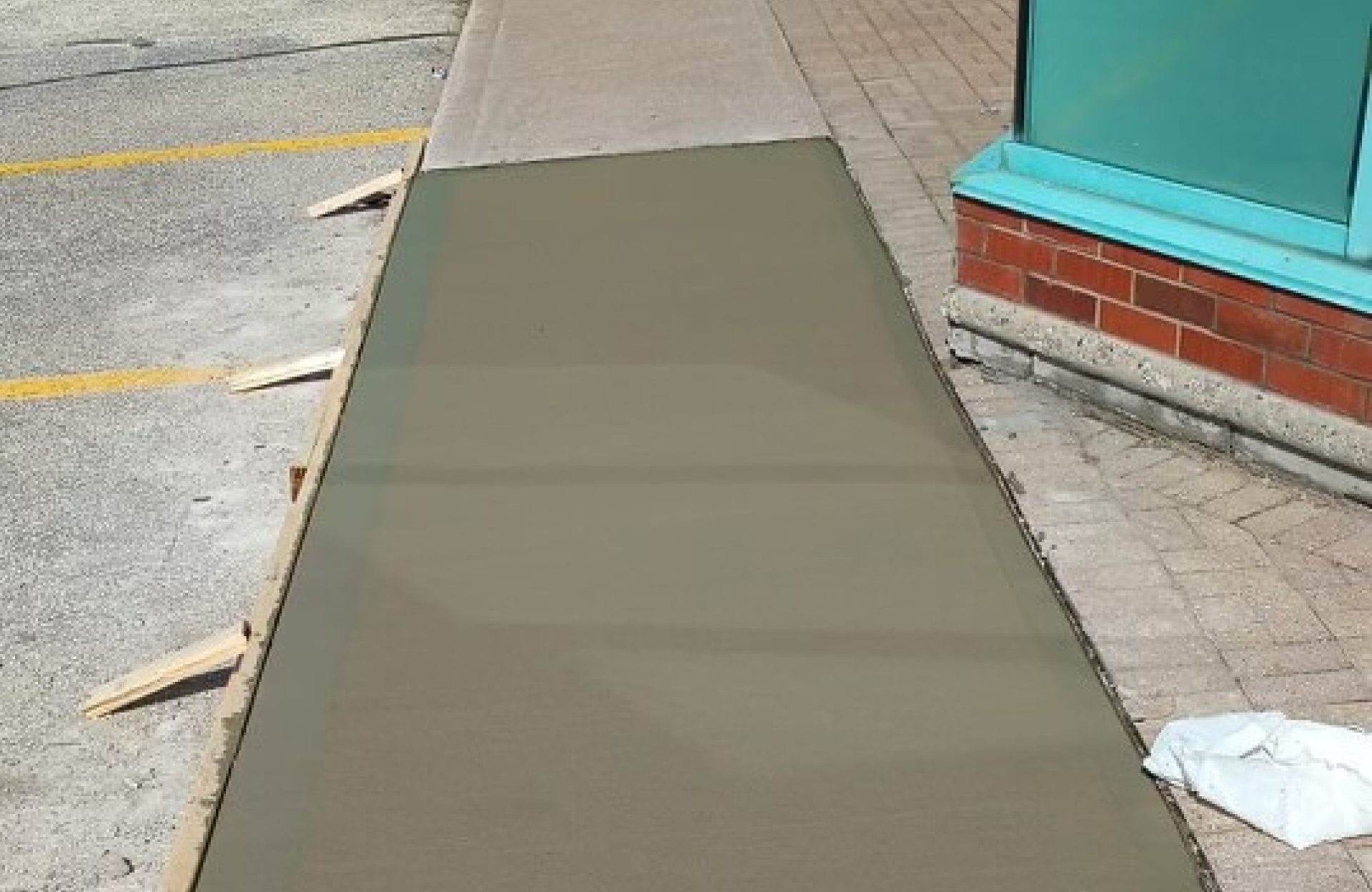 Seal Canada Fresh concrete has been poured onto a section of sidewalk next to a building, with wooden boards used to frame the edges, creating a neat boundary that contrasts with nearby asphalt paving. Asphalt & Coatings