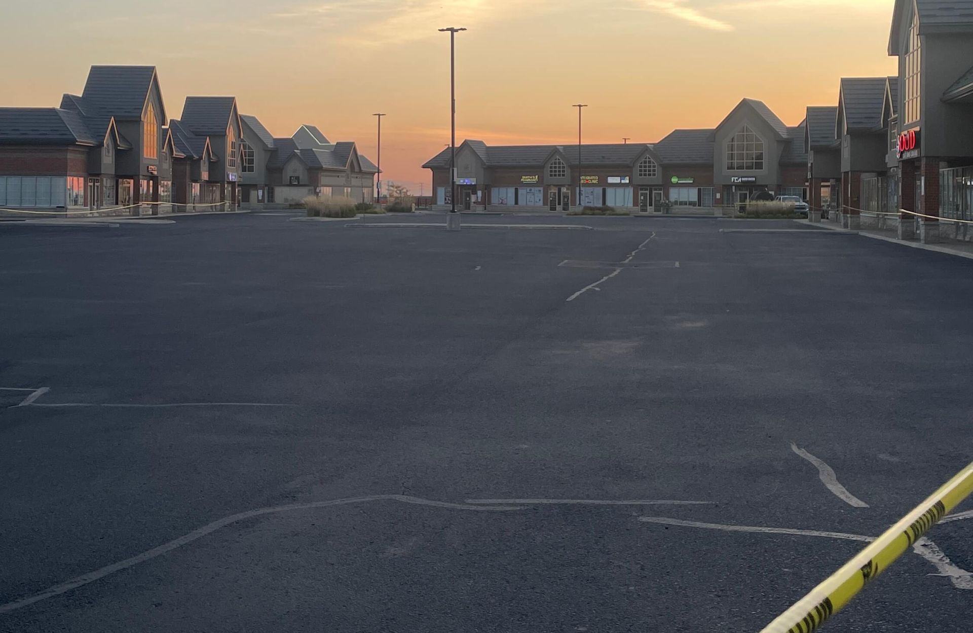 Seal Canada An empty parking lot with visible crack sealing in front of a shopping plaza at sunset. Asphalt & Coatings