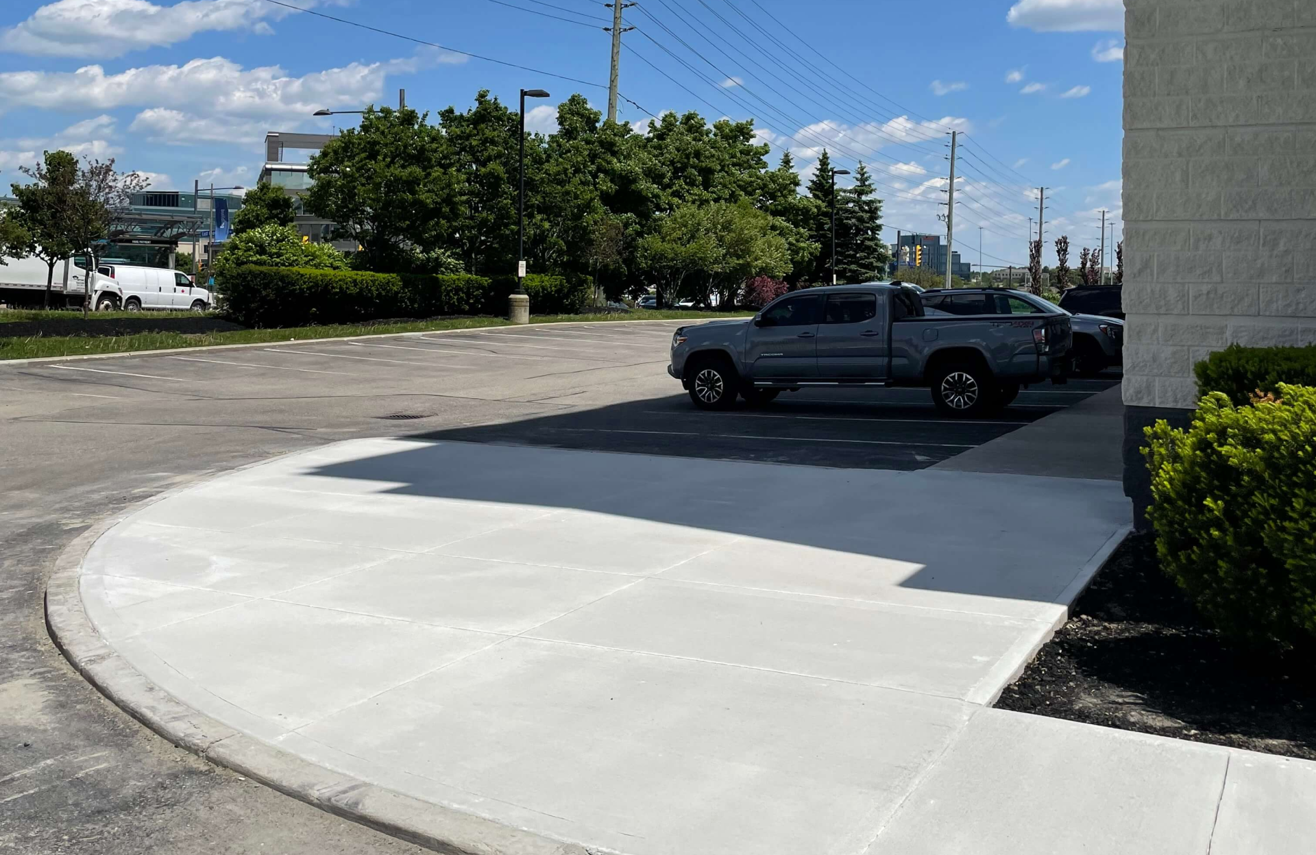 Seal Canada A concrete sidewalk in the foreground leads to an asphalt parking lot, enhancing curb appeal for commercial properties with a parked gray pickup truck under a clear sky. Asphalt & Coatings