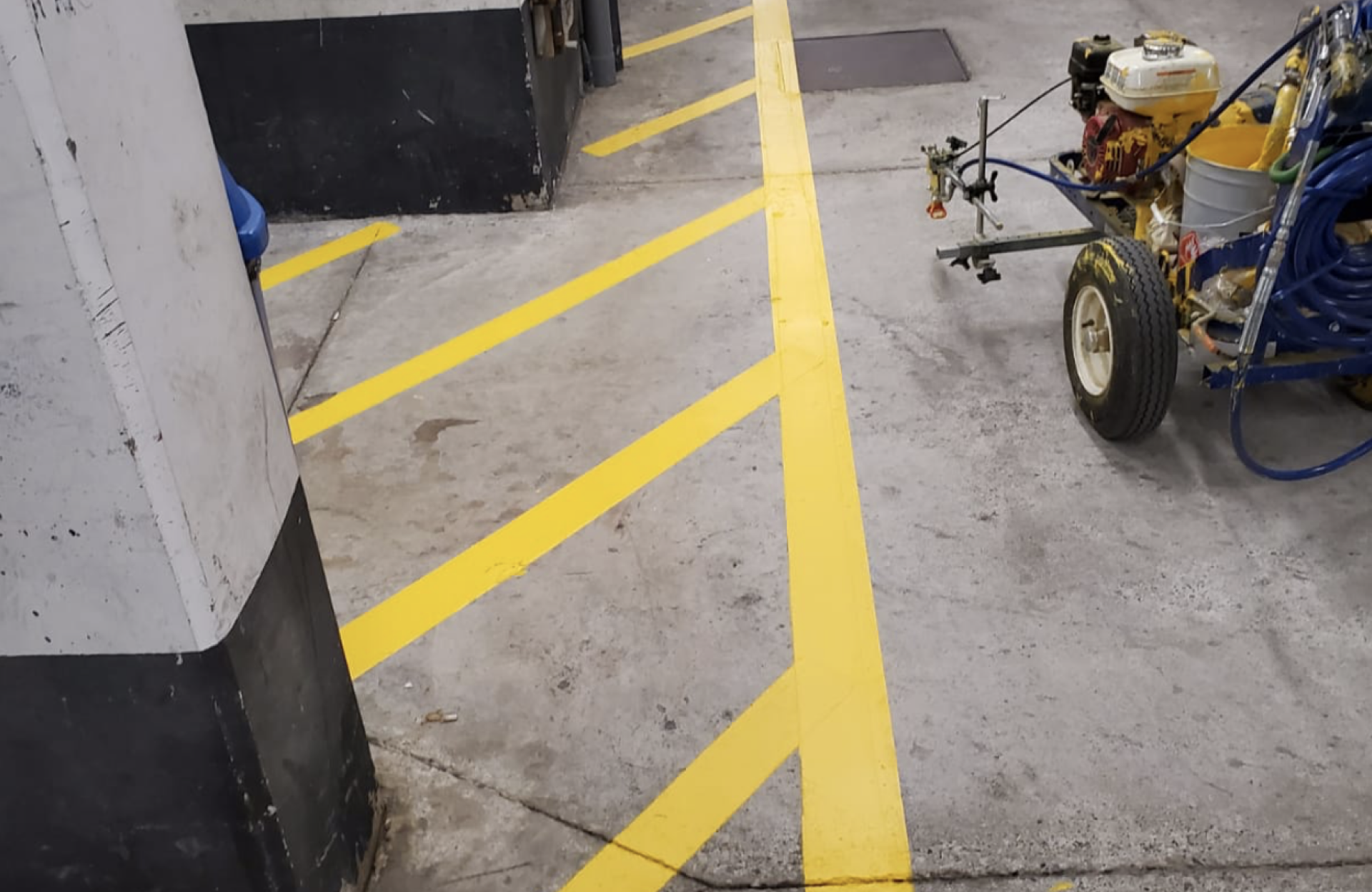 Seal Canada A yellow line painting machine parked on a concrete floor next to freshly painted yellow safety lines. Asphalt & Coatings